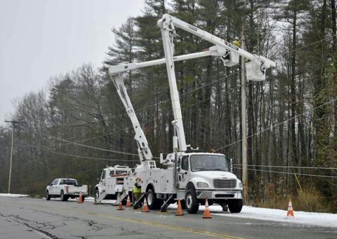 Unitil trucks raise bucket to fix wires with trees in background
