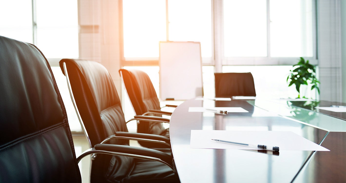 Large office table surrounded by chairs with sunlight shining through windows