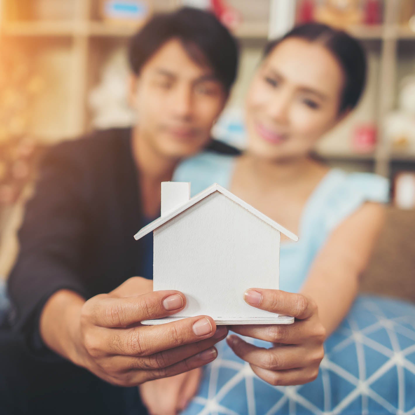 young couple sitting on couch and holding a wooden house in their hands