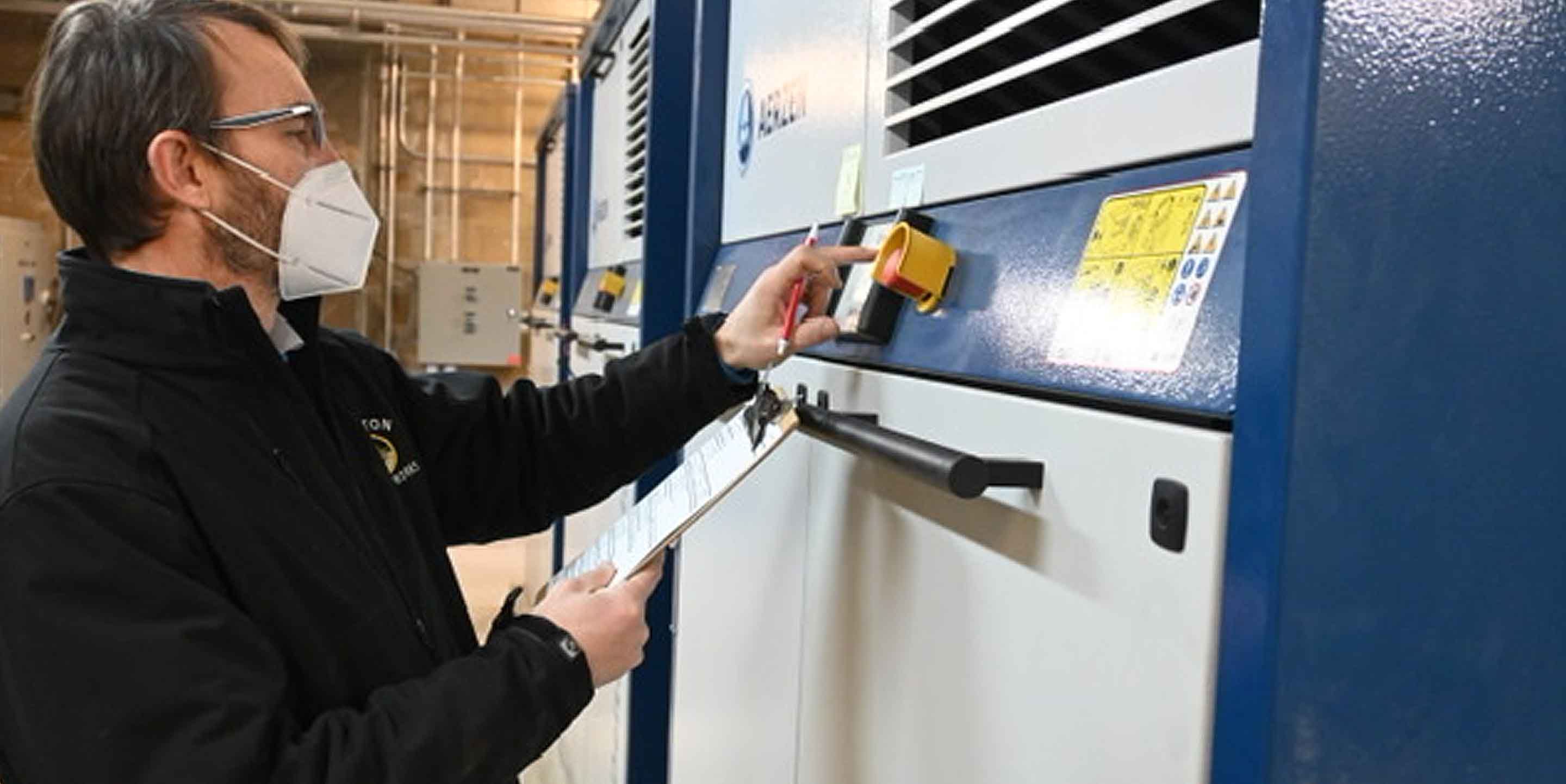 a wastewater plant employee stands with clipboard in front of new machine