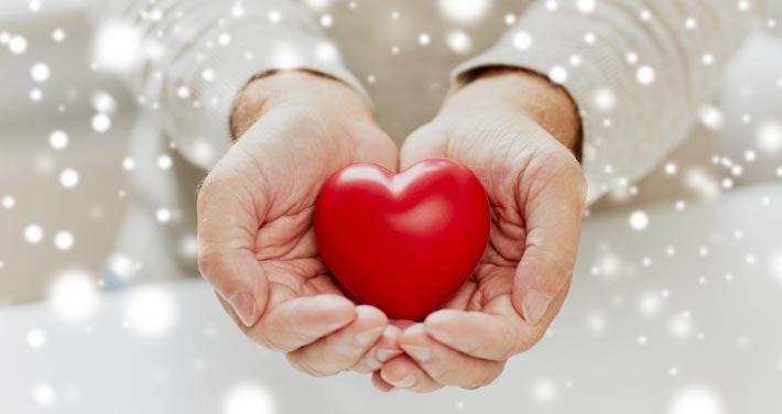 hands holding a plastic heart symbol with snowflakes in foreground