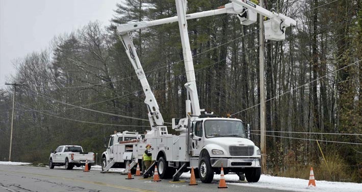 Unitil trucks raise bucket to fix wires with trees in background