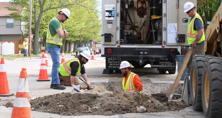 workers in and surrounding an excavation site in the street blocked by street cones