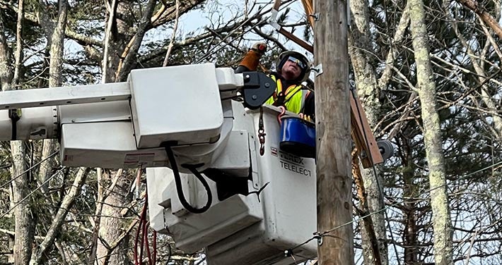 worker in bucket truck fixing utility pole with trees in background