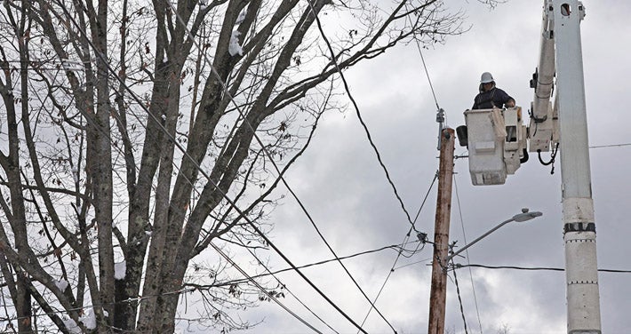 utility worker in bucket at top of utility pole with trees in background