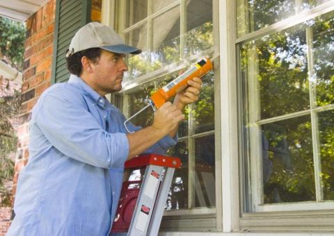 man on ladder caulking window