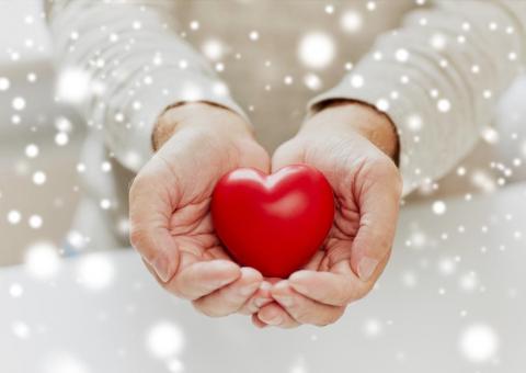 hands holding a plastic heart symbol with snowflakes in foreground