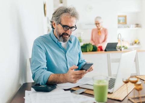 senior man using calculator at kitchen table