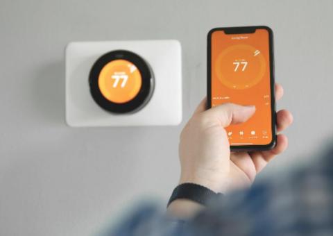 person holding smart phone in front of smart thermostat