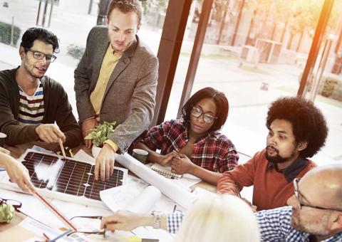 A business team sits around a table looking at a solar panel