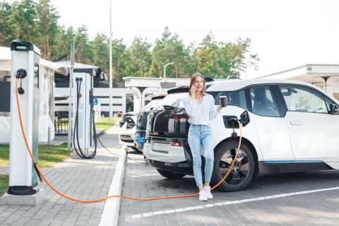 woman with a coffee leaning against a charging car