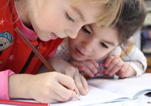 two young kids focusing on writing in a book