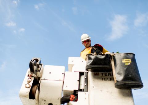 Lineworker looking down from a bucket against a blue sky