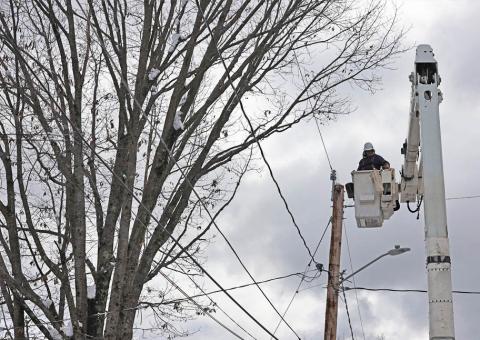 utility worker in bucket at top of utility pole with trees in background