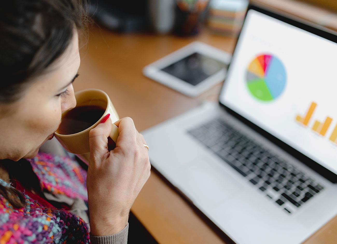 Woman at home sipping coffee and looking at graphs on laptop